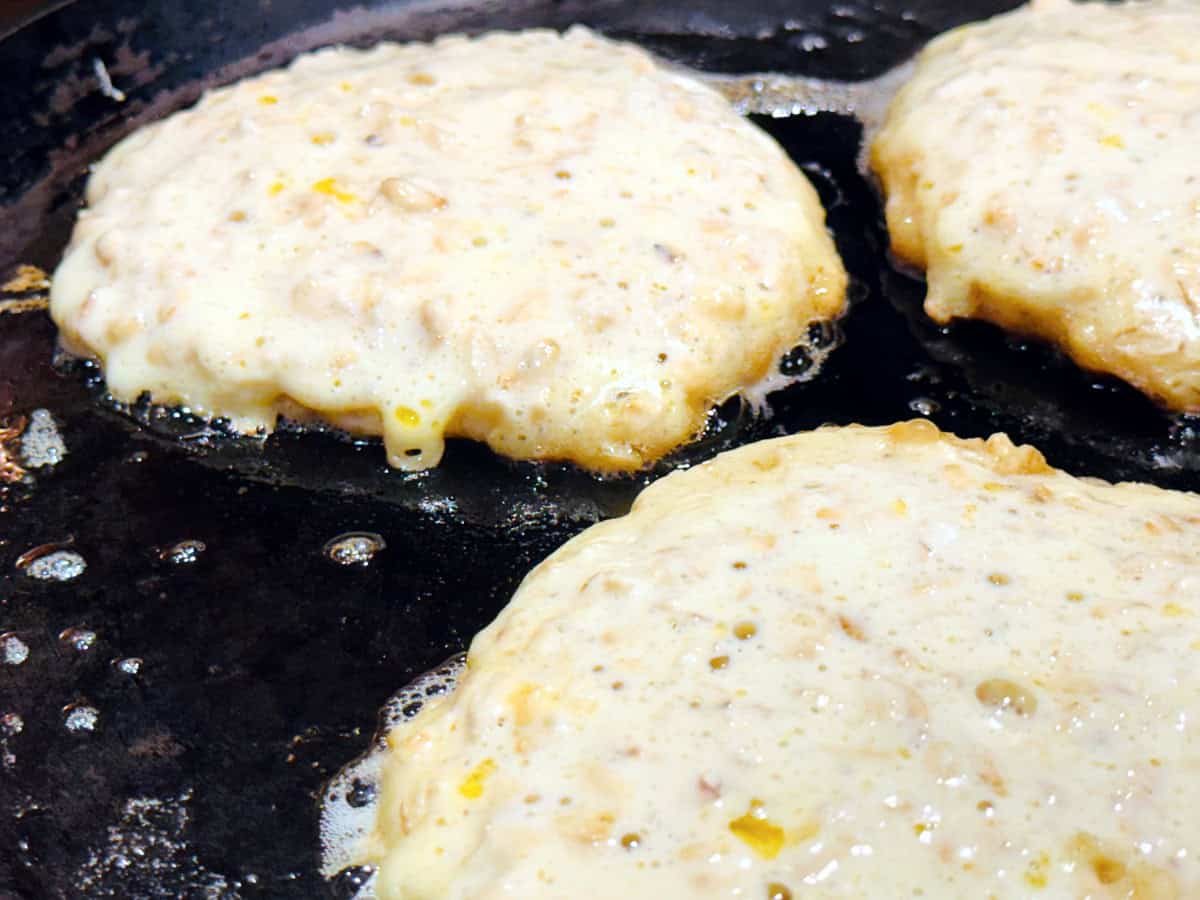 Three puddles of pancake batter cooking on a cast iron griddle.