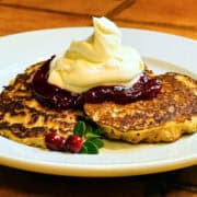 Oatmeal pancakes topped with lingonberry sauce and whipped cream on a white plate.