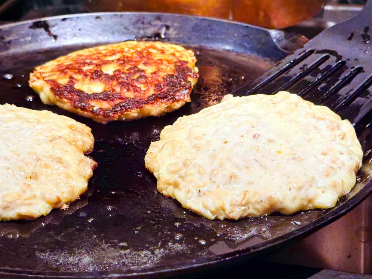 Pancakes being flipped with a black spatula on a cast iron griddle.