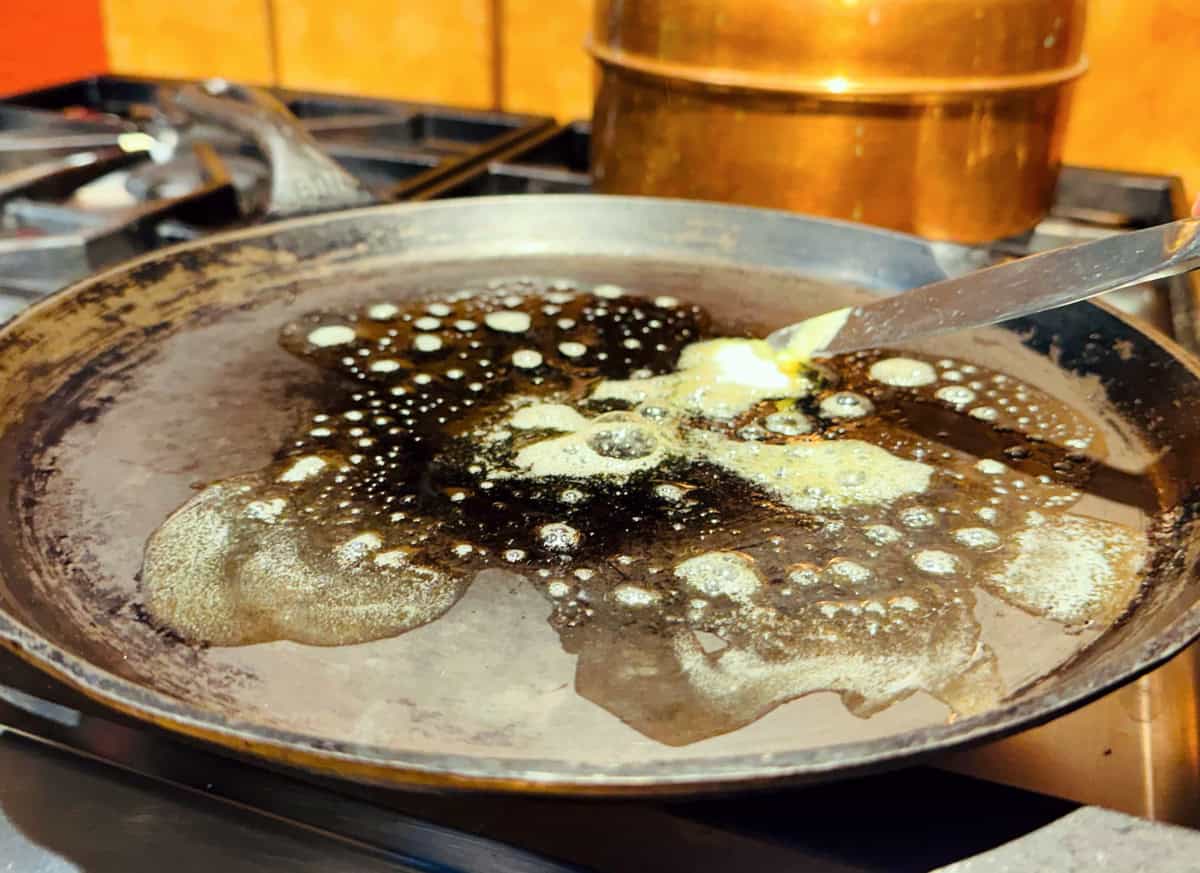 Butter melting on a round cast iron griddle sitting on the stove.