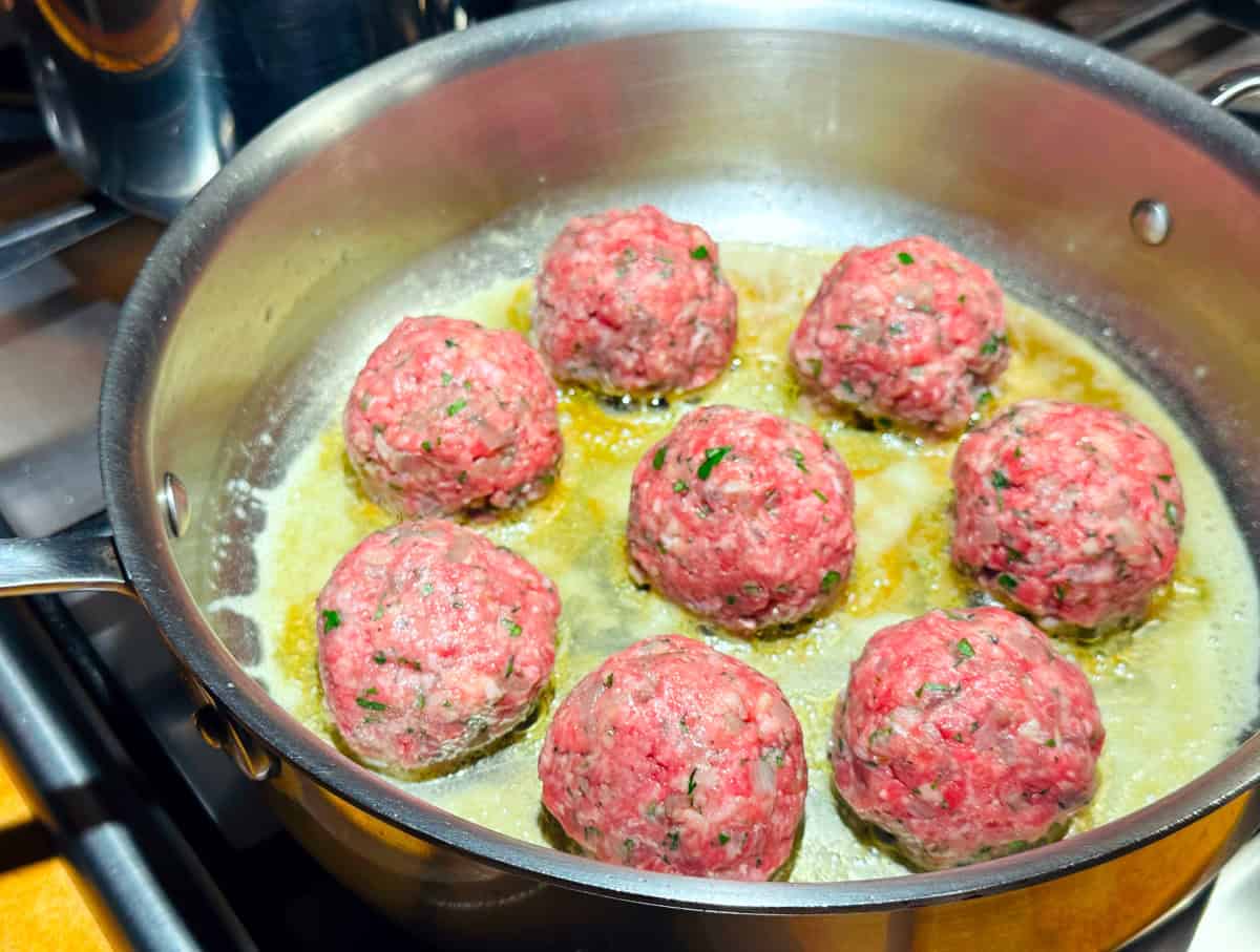 Meatballs cooking in melted butter in a deep sided steel saute pan.