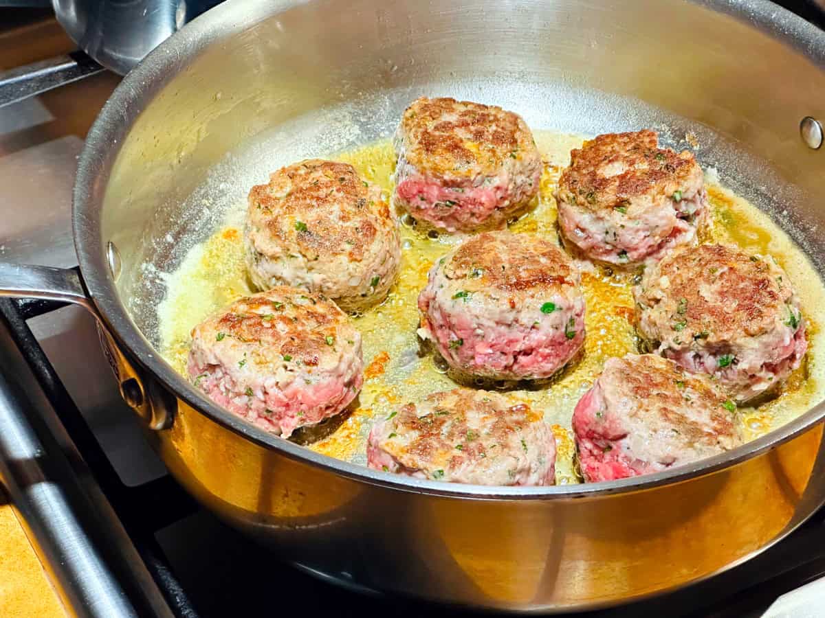 Meatballs browning in a deep sided steel sauce pan.