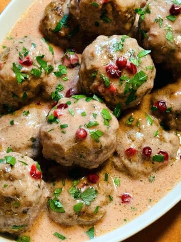 Swedish meatballs sprinkled with chopped parsley in a white serving dish.