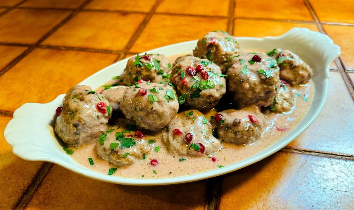 Swedish meatballs sprinkled with chopped parsley in a white serving dish.