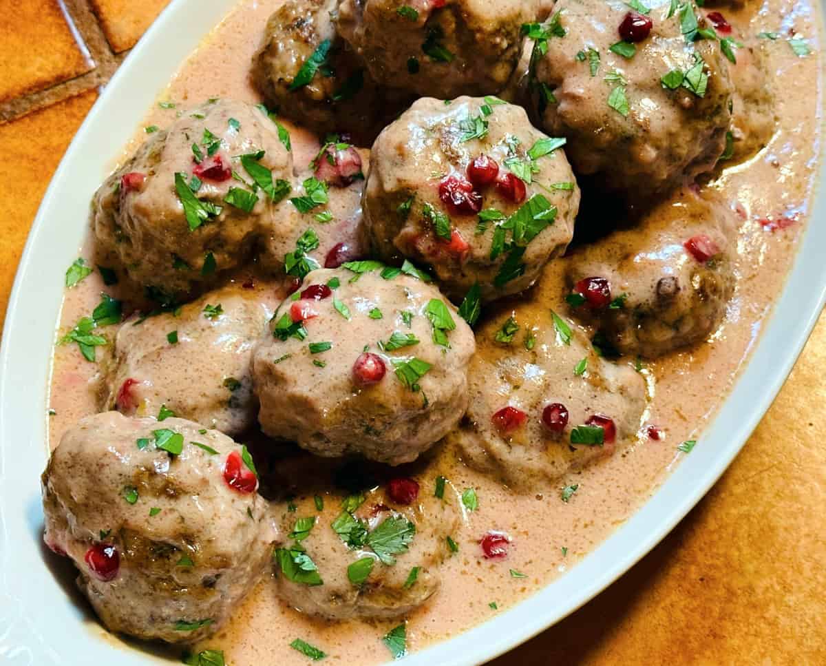 Swedish meatballs sprinkled with chopped parsley in a white serving dish.