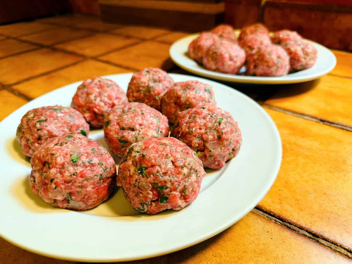 Raw meatballs sitting on two white plates.