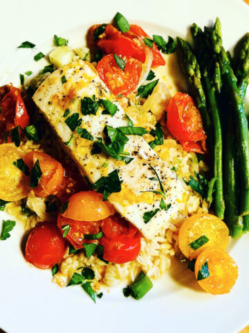 Halibut provencal on a white plate with a side of asparagus.