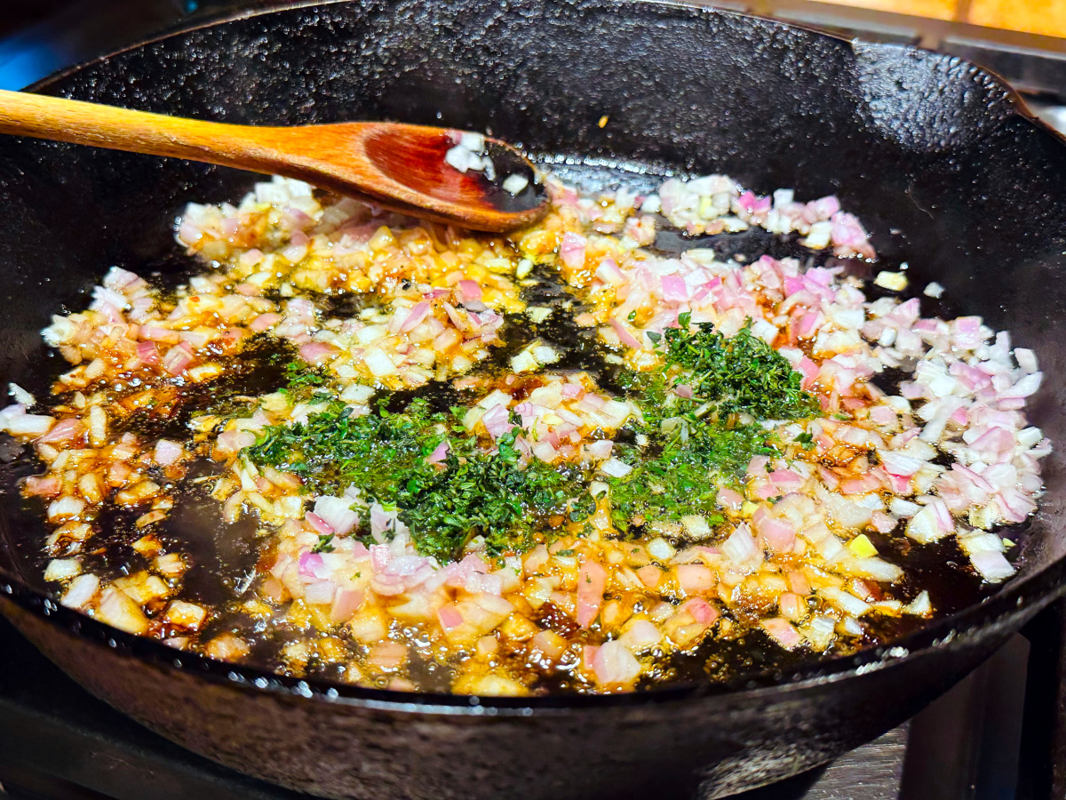 Chopped fresh thyme sitting on chopped shallot cooking in a cast iron skillet.