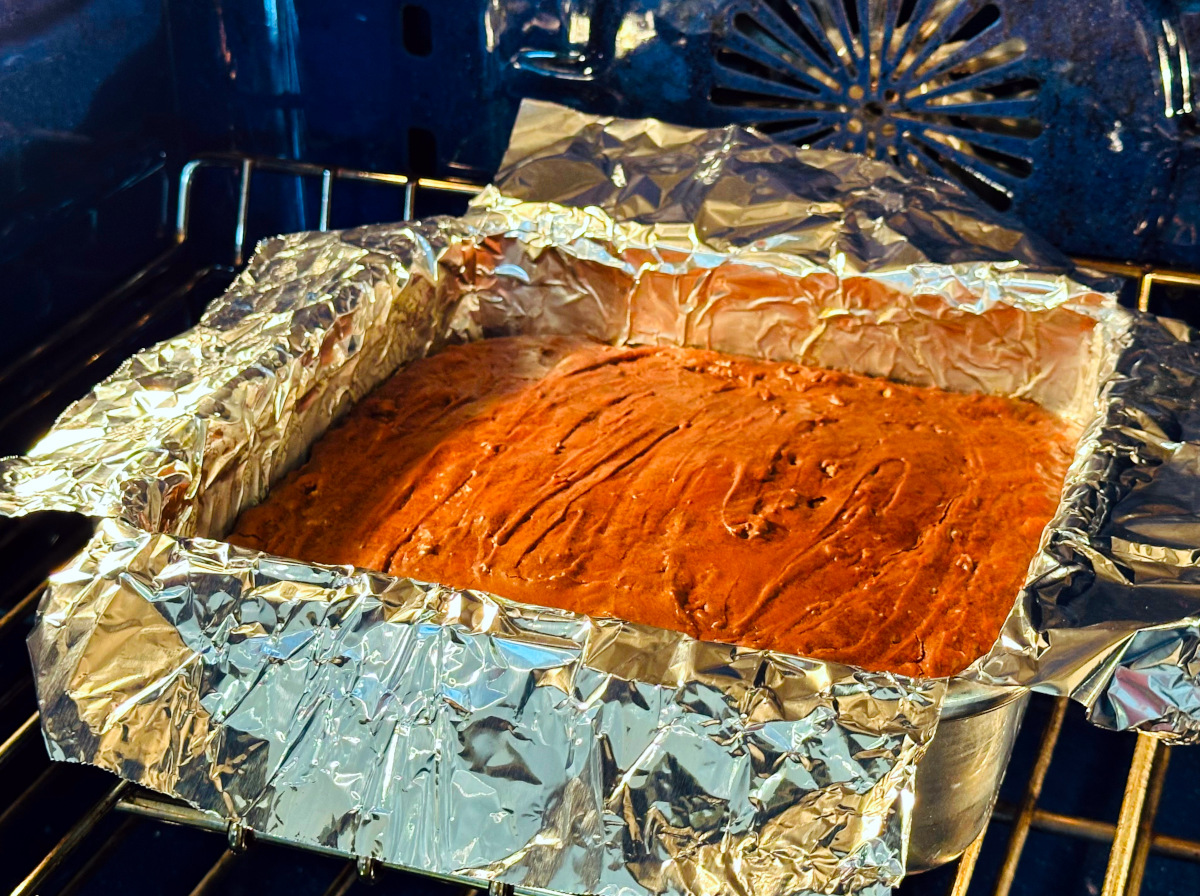 Fudgy brownies in a foil lined square pan baking in a blue oven.