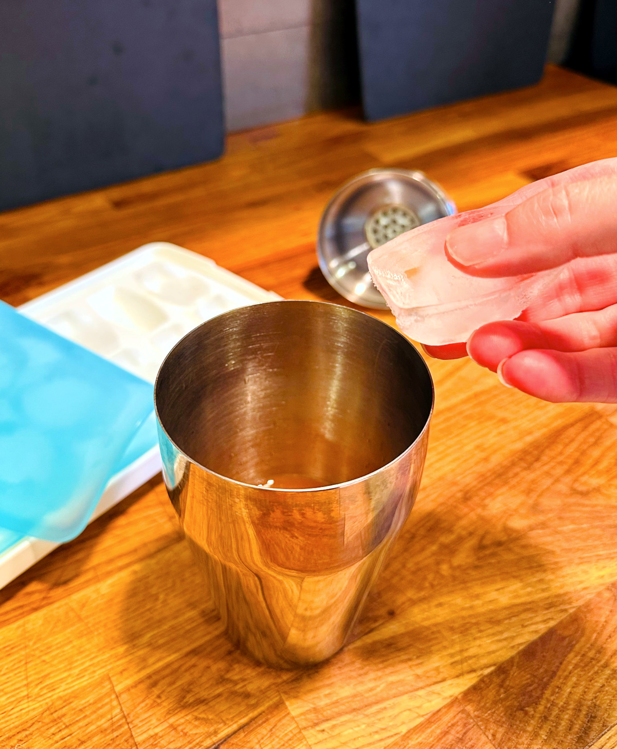 Ice cube being added to steel cocktail shaker.