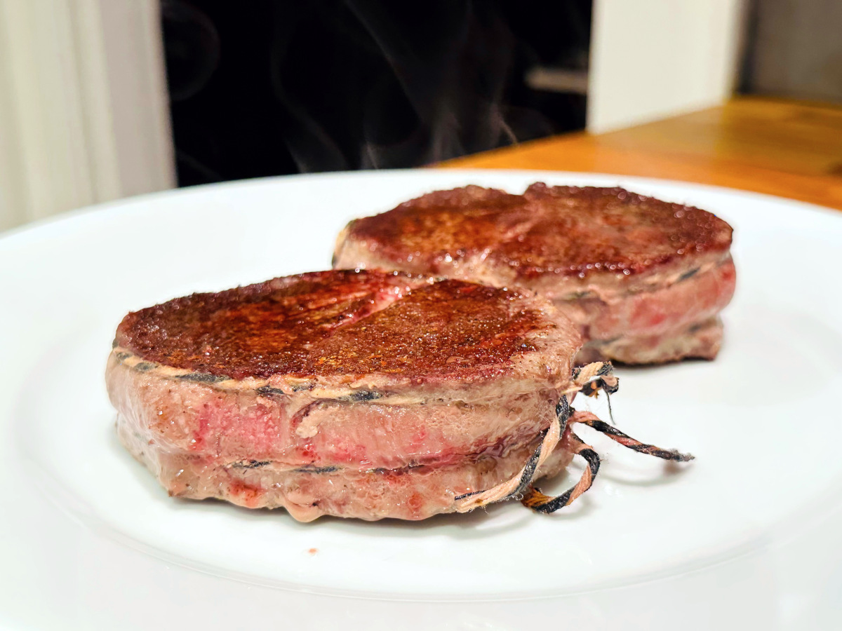 Two pan seared filet mignon steaks steaming and resting on a white plate.