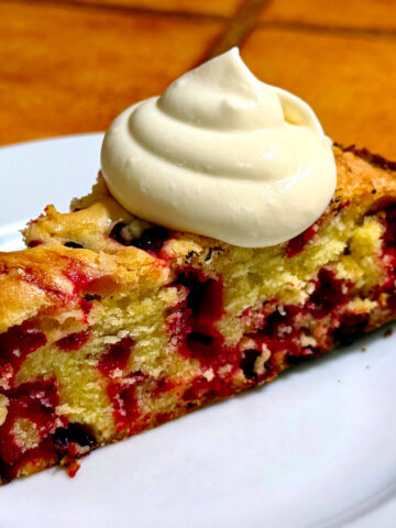 Cranberry cake with a dollop of whipped cream served on a small white plate.