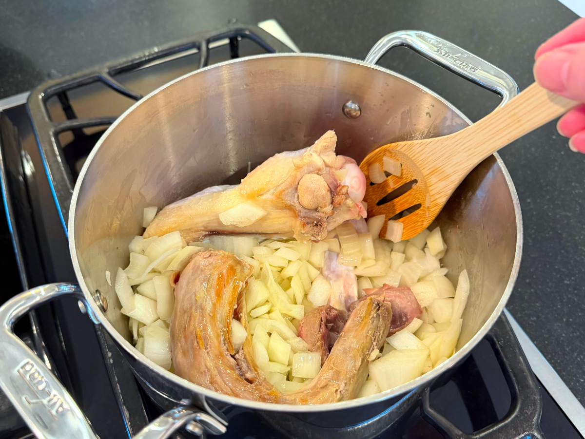 Turkey parts and chopped onion being browned in a steel saucepan.