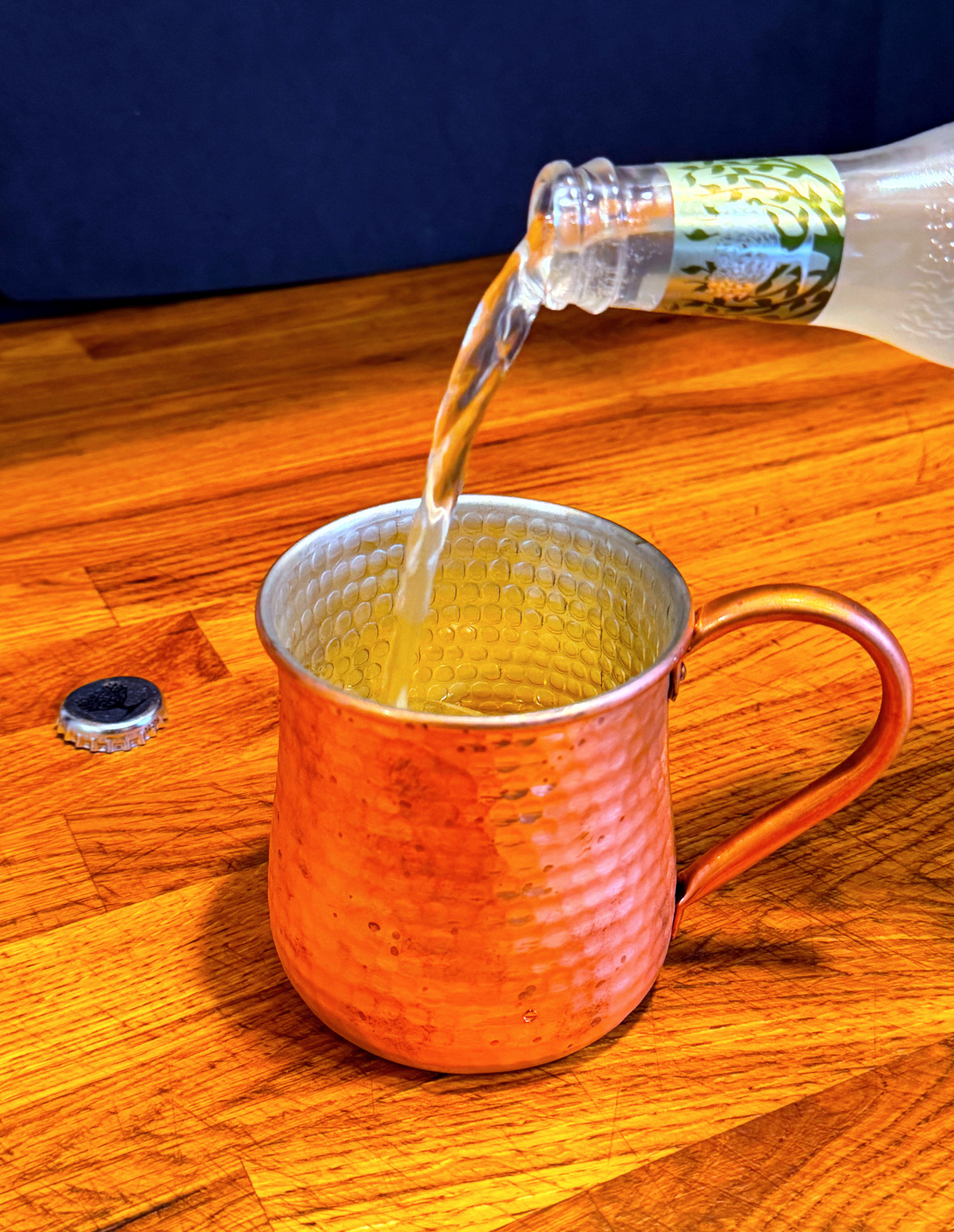 Pale liquid being poured from a bottle into a copper mug.