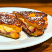 Monte Cristo sandwich sprinkled with powdered sugar and sliced in half on a white plate.