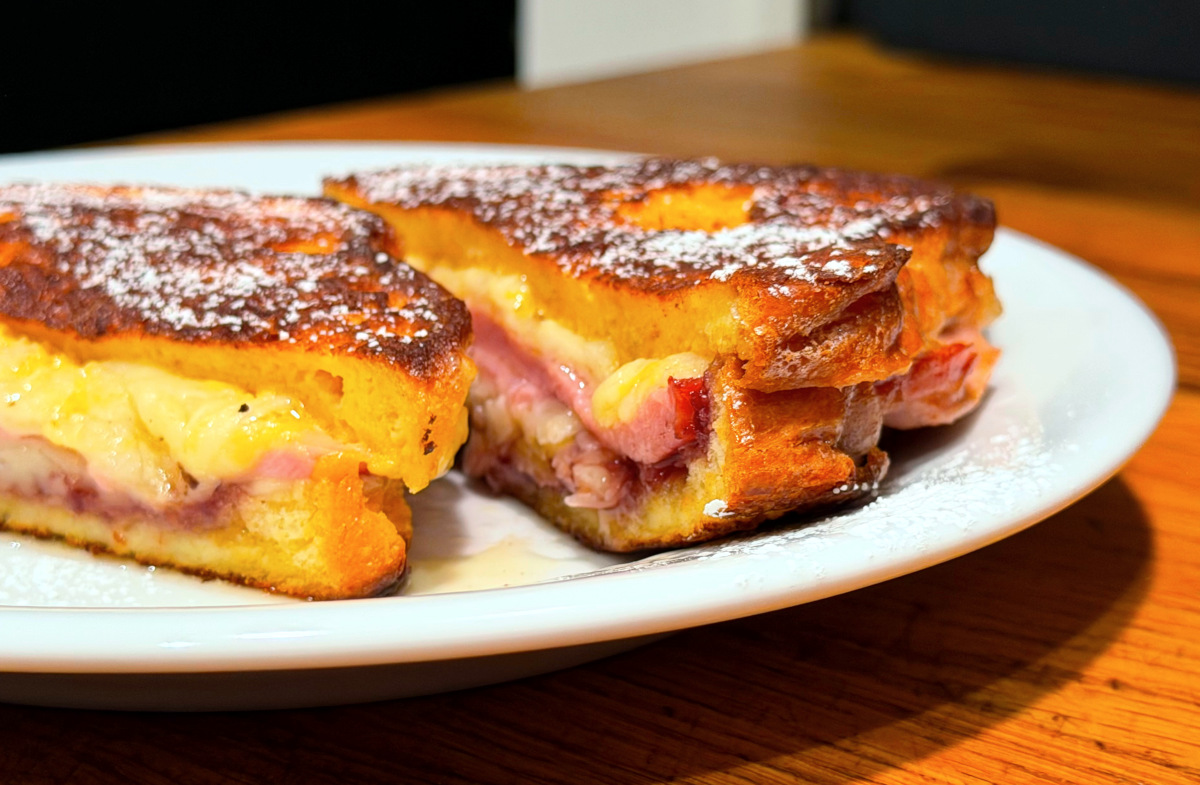Monte Cristo sandwich sprinkled with powdered sugar and sliced in half on a white plate.