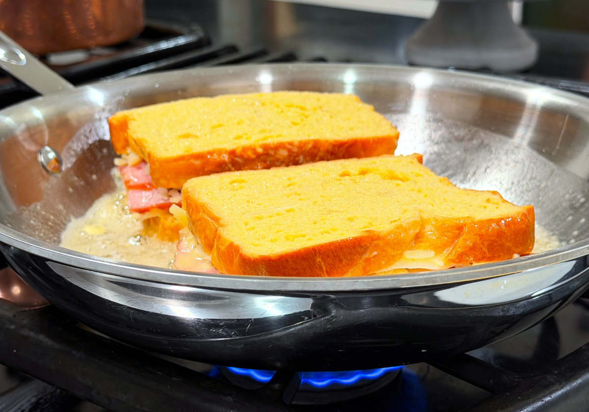 Two sandwiches frying in butter in a large steel frying pan.