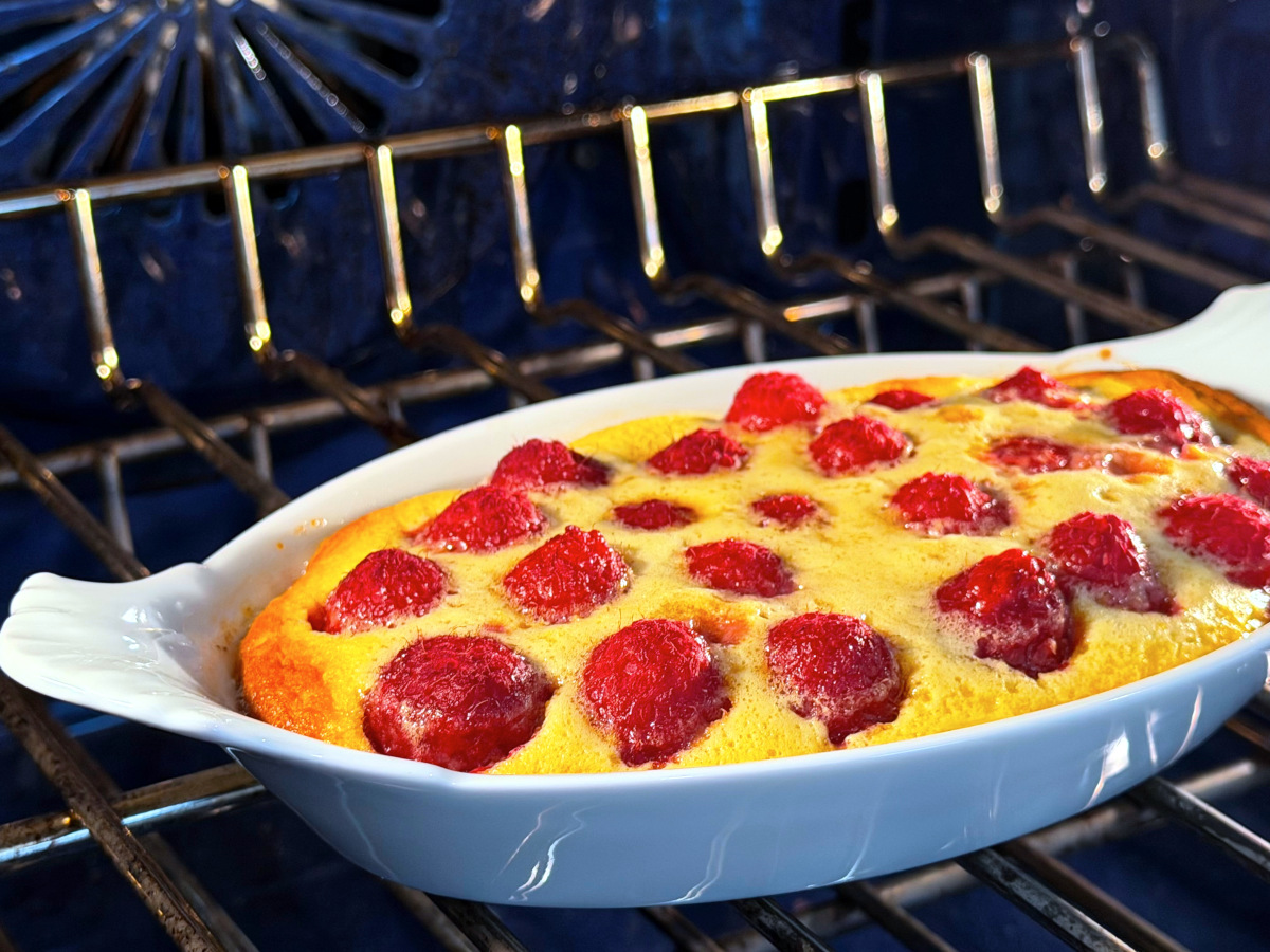 Raspberry flaugnarde in a white oval porcelain baking dish in a blue oven.