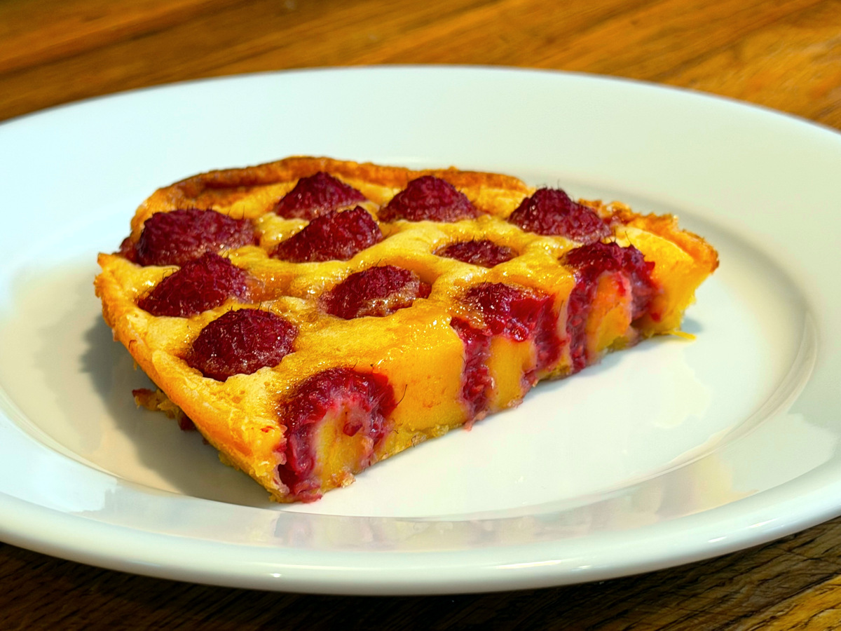 Slice of raspberry flaugnarde sitting on a white plate.