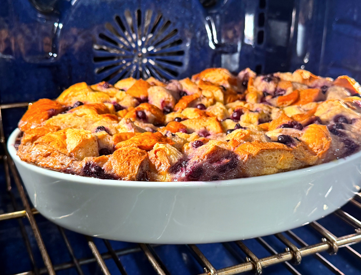 Blueberry bread pudding in a white baking dish sitting in a blue oven.