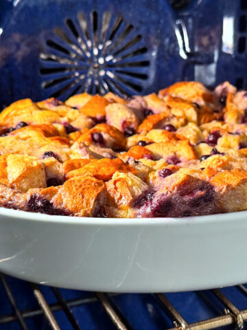 Blueberry bread pudding in a white baking dish sitting in a blue oven.