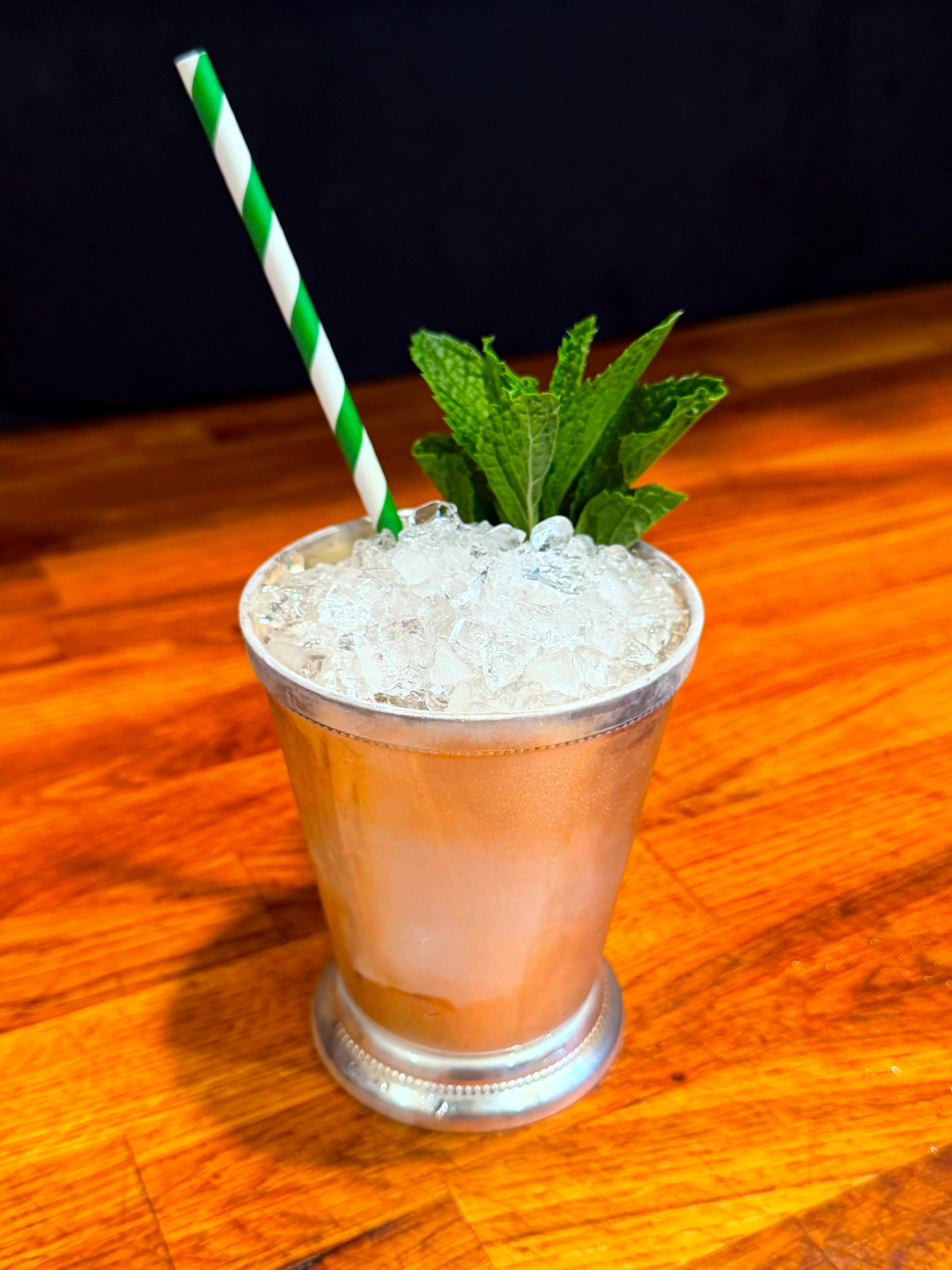 Mint julep served in a silver julep cup garnished with a sprig of mint next to a green and white striped straw.