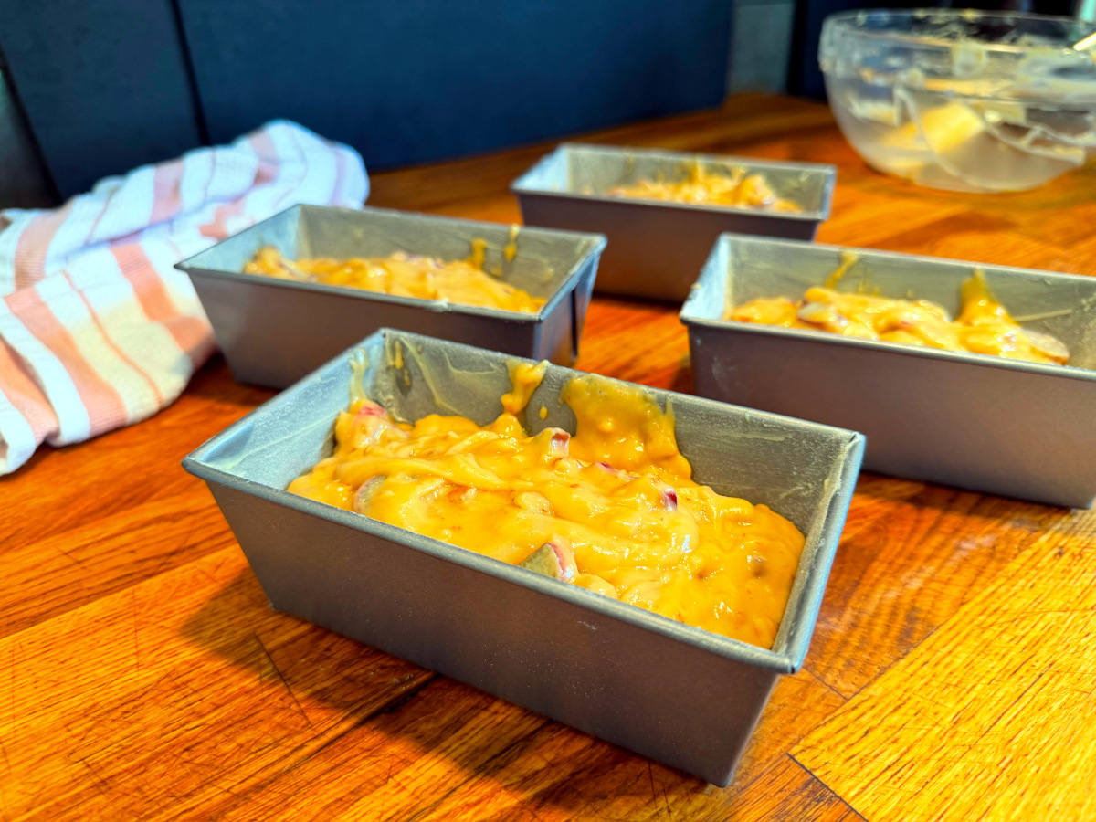 Four miniature loaf pans filled with batter sitting on a wood counter.