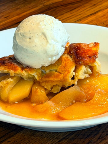 Apple pandowdy with a scoop of vanilla ice cream served in a shallow white bowl.