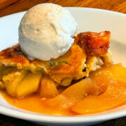 Apple pandowdy with a scoop of vanilla ice cream served in a shallow white bowl.