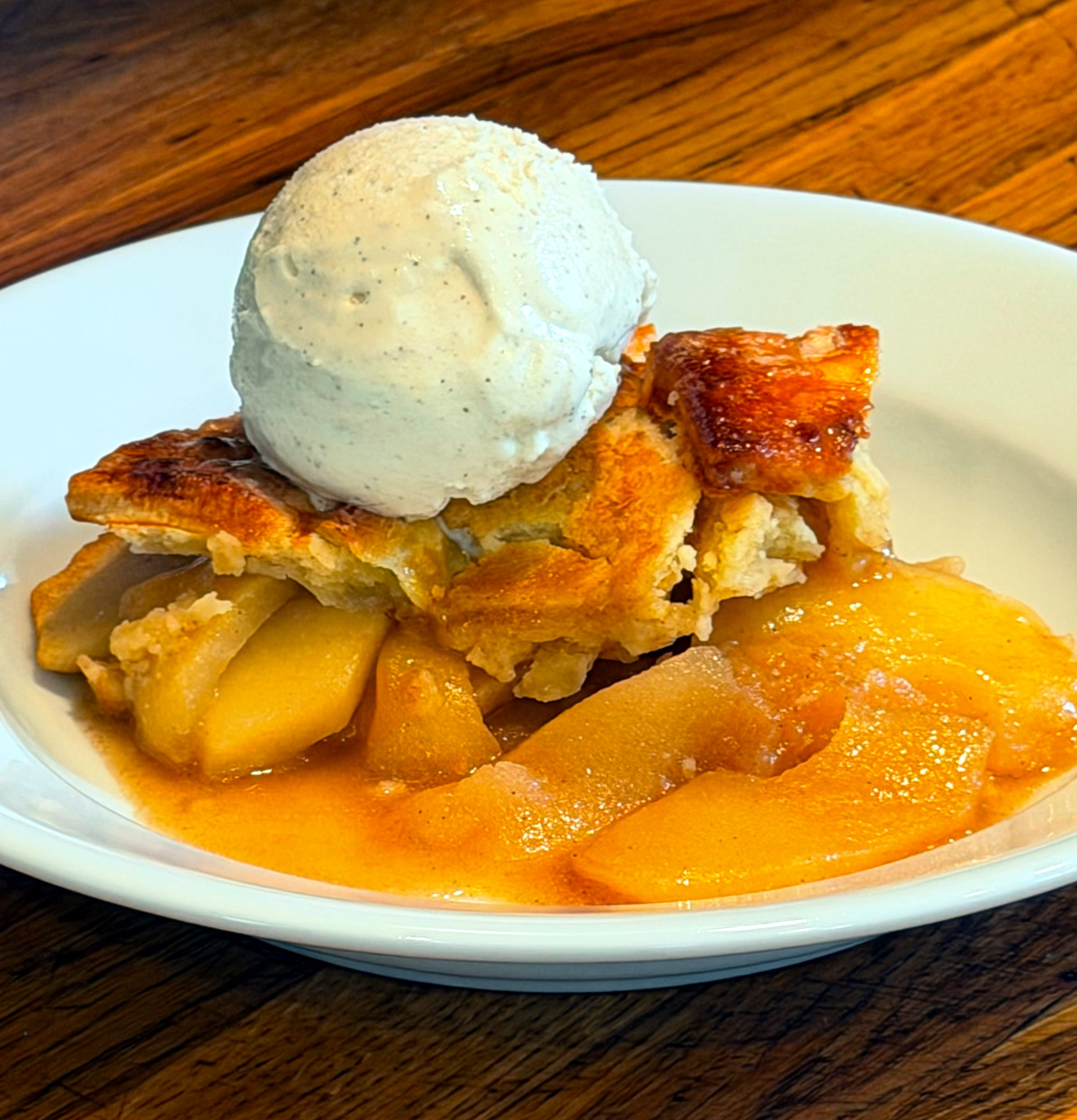 Apple pandowdy with a scoop of vanilla ice cream served in a shallow white bowl.
