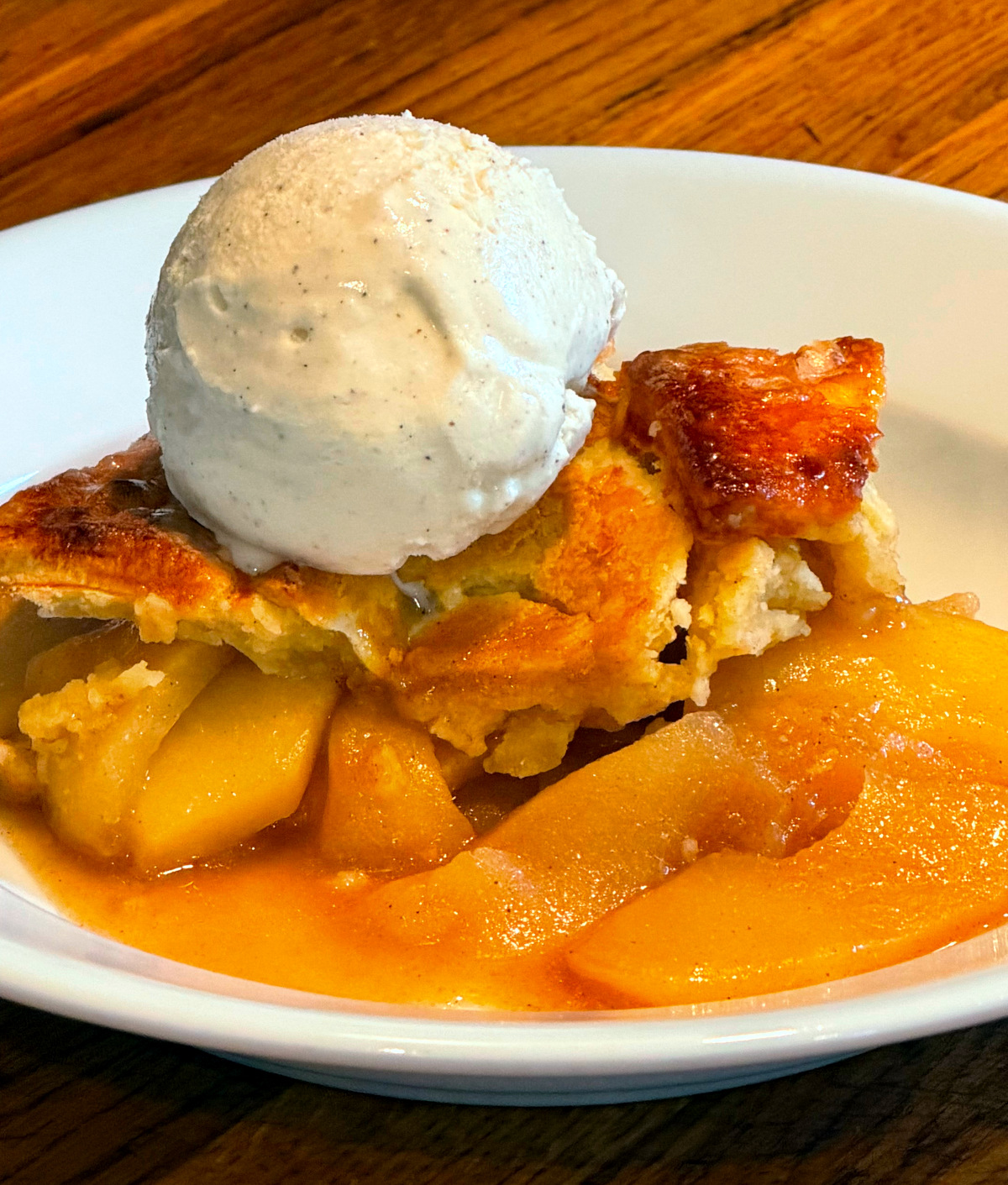 Apple pandowdy with a scoop of vanilla ice cream served in a shallow white bowl.