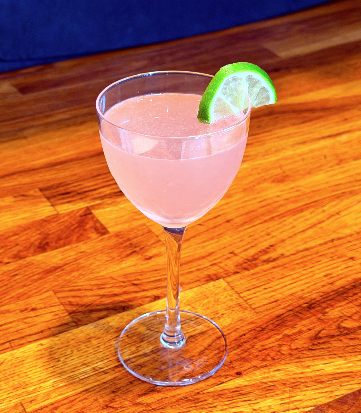 Pink palace cocktail served in a Nick and Nora glass garnished with a lime wedge.