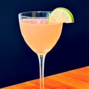 Pink palace cocktail served in a Nick and Nora glass garnished with a lime wedge.