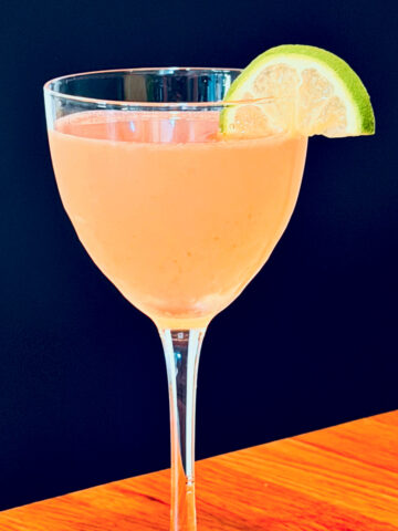 Pink palace cocktail served in a Nick and Nora glass garnished with a lime wedge.