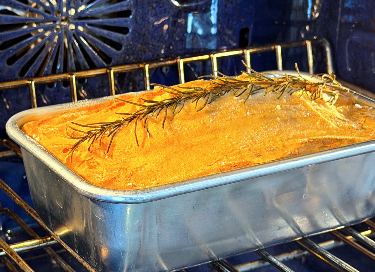 Apple rosemary remembrance cake baking in a loaf pan in a blue oven.