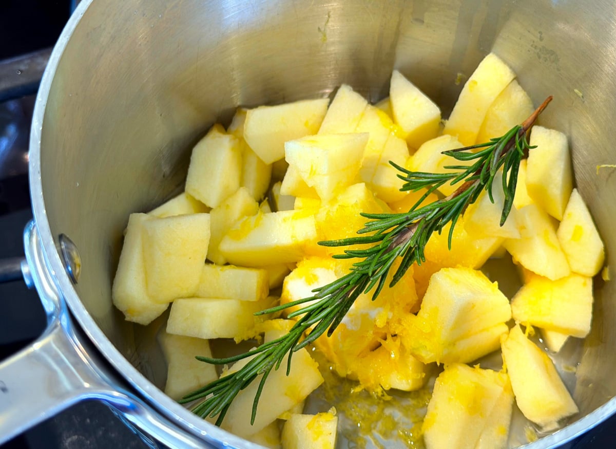 Chopped apples, lemon zest, and a rosemary sprig in a small steel saucepan.