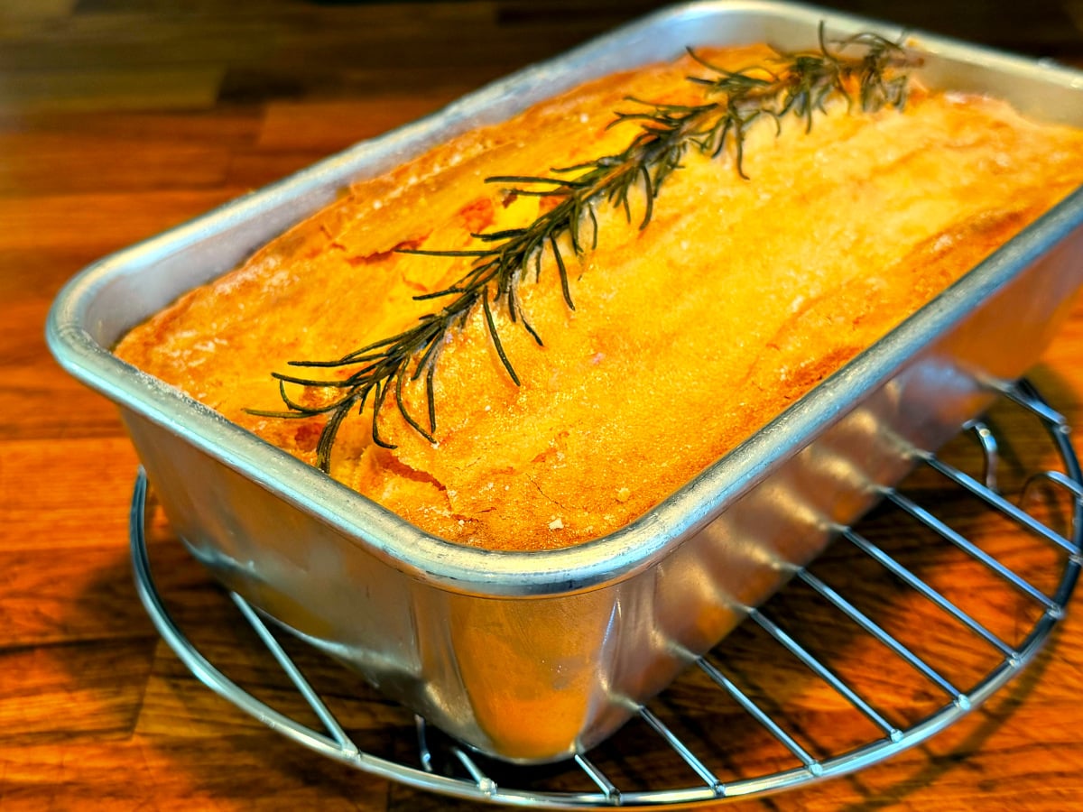 Apple rosemary remembrance cake cooling in a metal loaf pan on a wire rack.