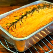 Apple rosemary remembrance cake in a metal loaf pan cooling on a wire rack.