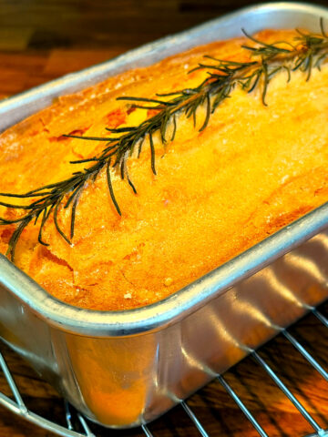 Apple rosemary remembrance cake in a metal loaf pan cooling on a wire rack.