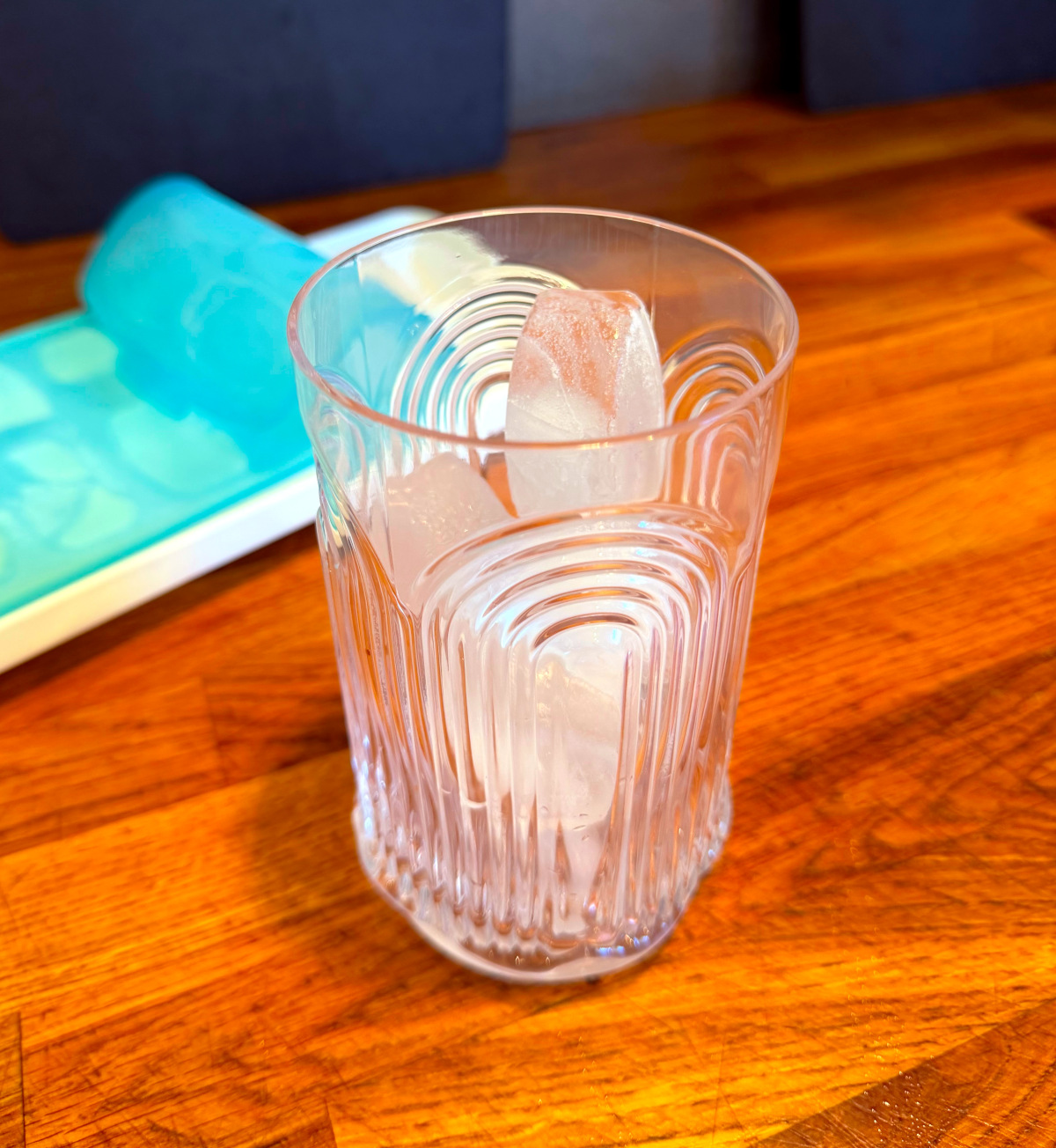 Tall etched glass full of ice cubes next to an ice cube tray with a light blue lid.