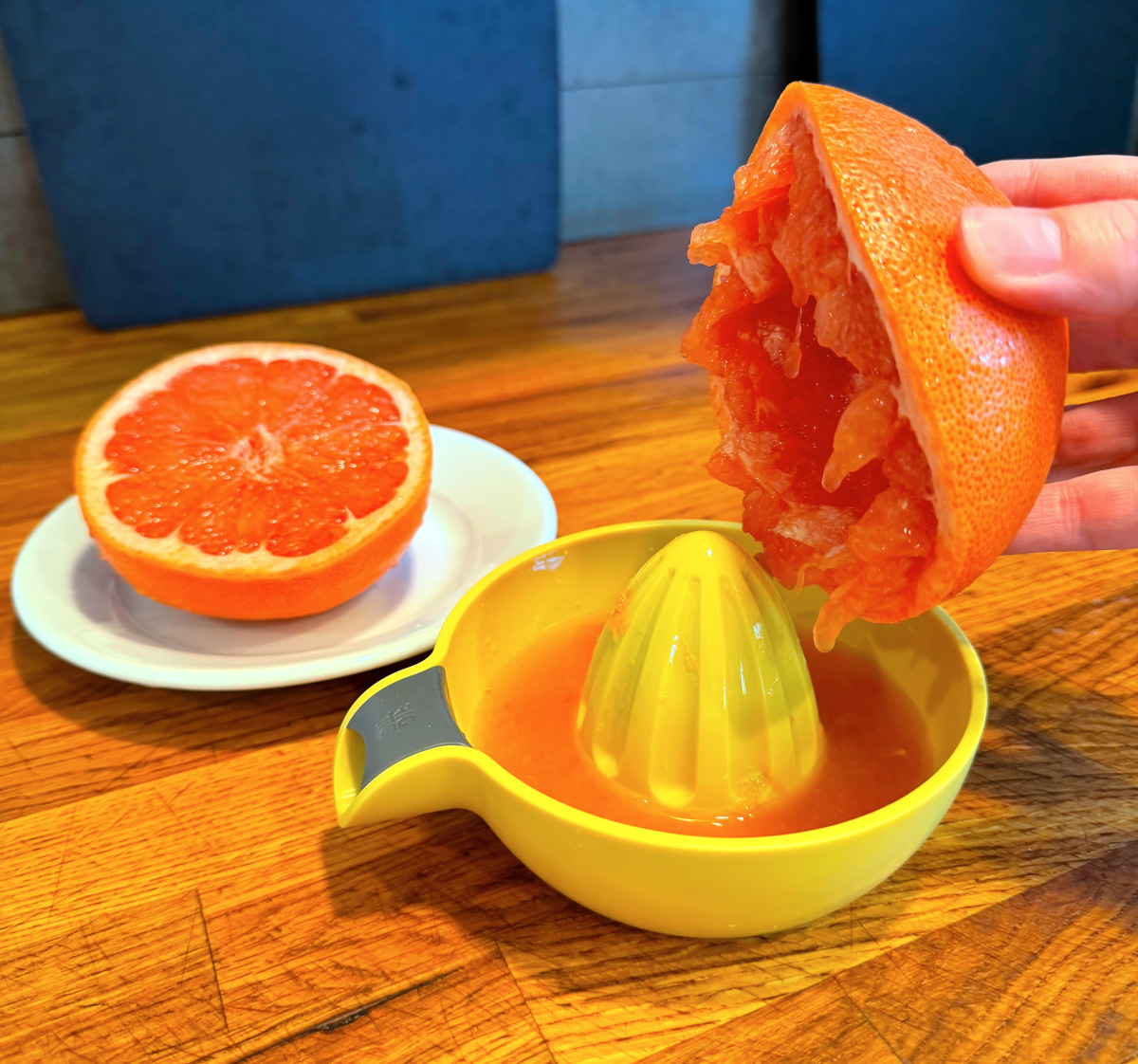 Fresh grapefruit being juiced on a yellow plastic juicer next to half a grapefruit sitting on a small white plate.